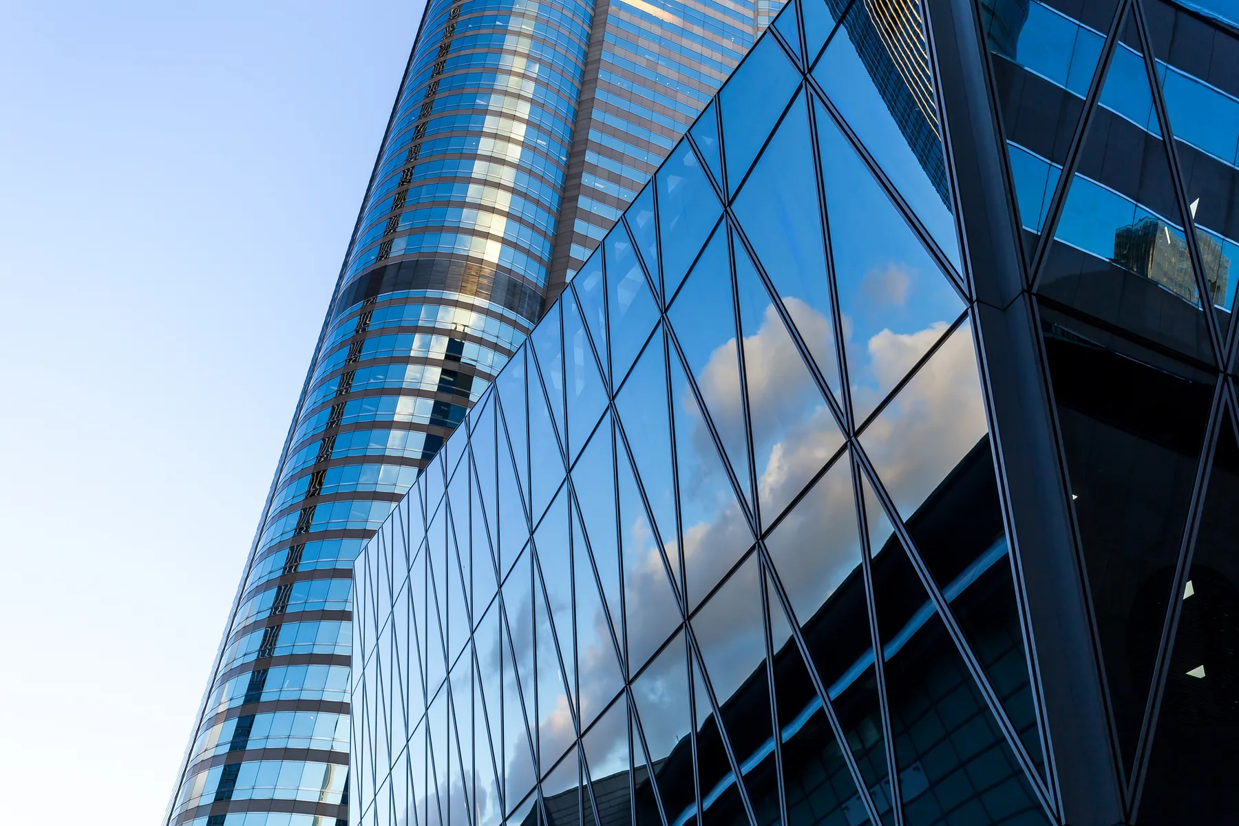 A curved glass tower reflecting the sky, looking up