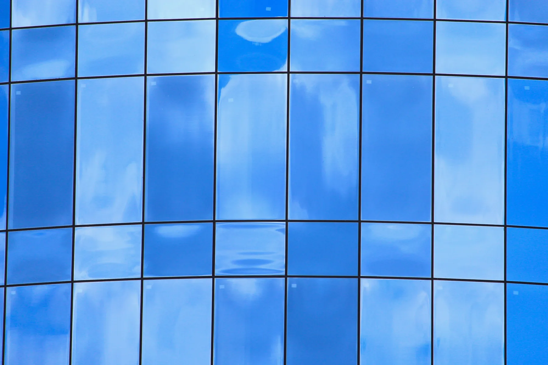 A curved blue glass grid reflecting clouds