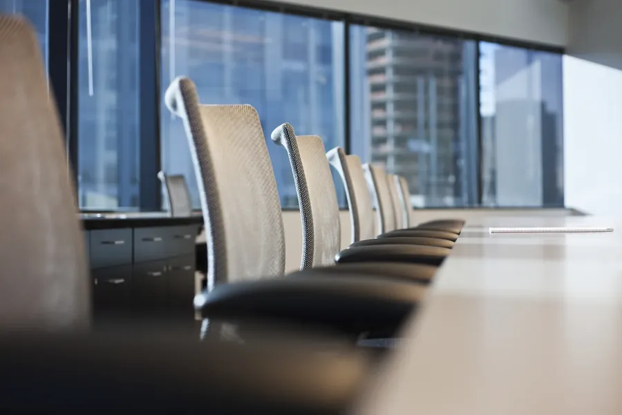 An empty boardroom table and chairs, a city view beyond